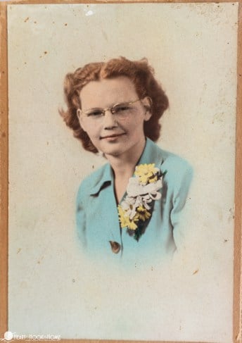 Old Portrait of a woman wearing a blue shirt and flowers pinned to her shirt.
