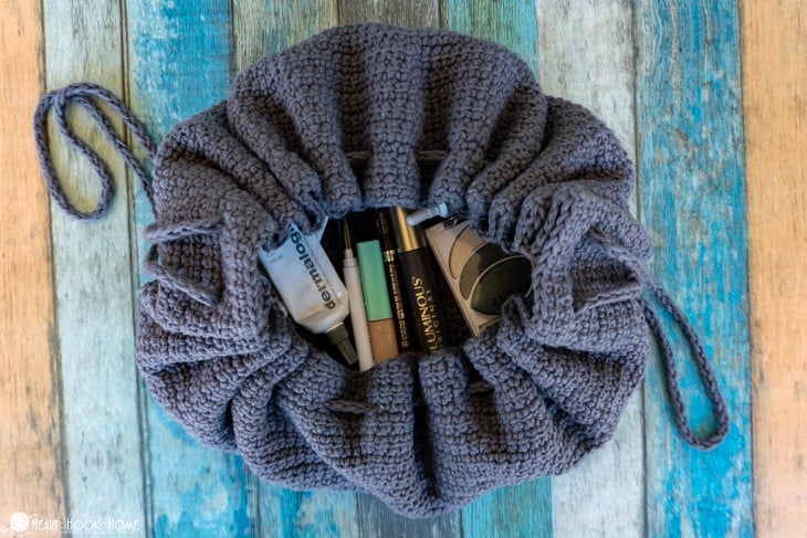 Example of a partially open, gray Drawstring Cosmetics Bag crochet pattern with various make up containers inside.
