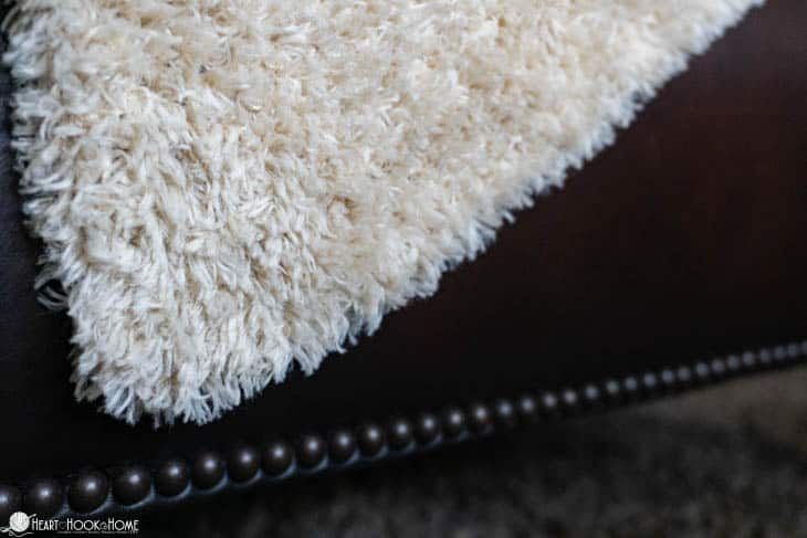 White example of the Faux Fur Throw crochet pattern draped over a leather couch.